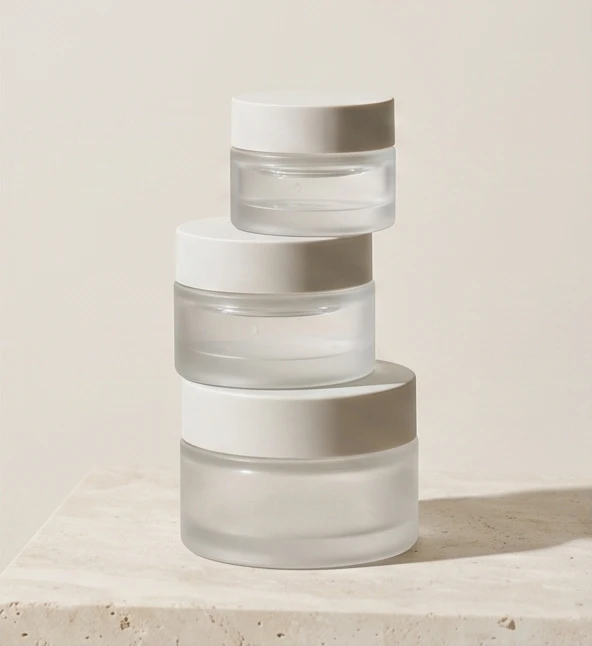 Three stacked frosted skincare jars in a calm warm-white setting
